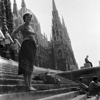 Woman posing on cathedral steps with suitcase.