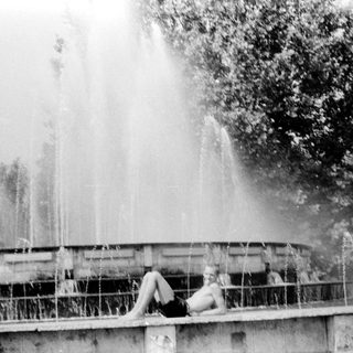Person lounging on fountain edge near waterfall.