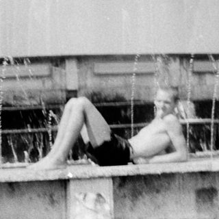 Person lounging on fountain edge near waterfall.