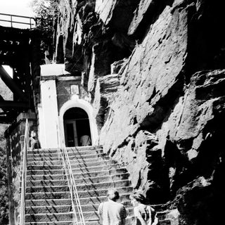 Staircase leading to cliffside building with bridge above.