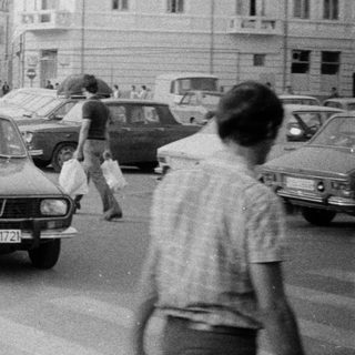 Vintage urban street scene with parked cars and pedestrians.