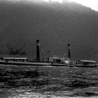 Steamship navigating through rough waters near mountainous shore.