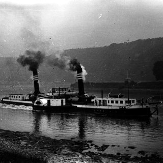 Steam-powered paddlewheel boat on river.