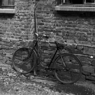 Vintage photo of couple standing by brick house with motorcycle and bicycle.