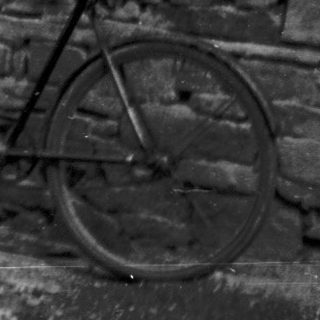 Vintage photo of couple standing by brick house with motorcycle and bicycle.