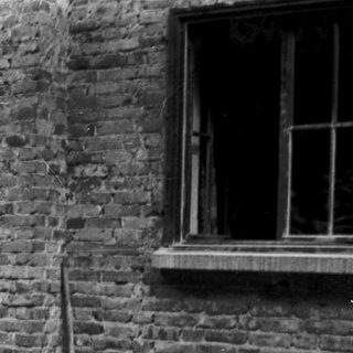 Vintage photo of couple standing by brick house with motorcycle and bicycle.