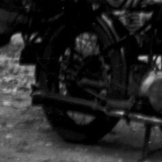Vintage photo of couple standing by brick house with motorcycle and bicycle.