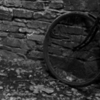 Vintage motorcycle with rider and woman standing by brick house.