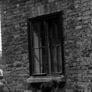 Vintage motorcycle with rider and woman standing by brick house.