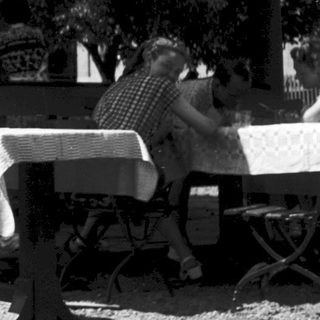 Outdoor pavilion with sign "Der Gäste Trunk in Freude" and seated patrons.