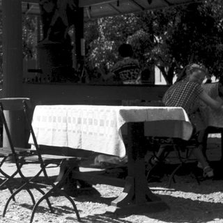 Outdoor pavilion with sign "Der Gäste Trunk in Freude" and seated patrons.