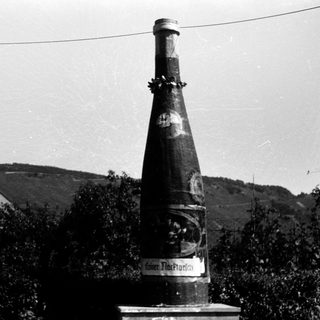 Large vintage wine bottle monument labeled "Kellerei Thiergarten" outdoors.