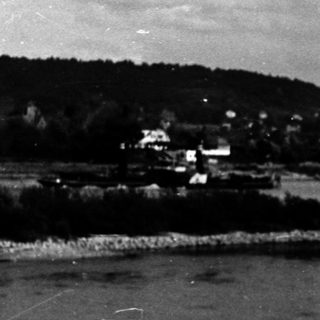Coastal village by calm waterfront with hills.