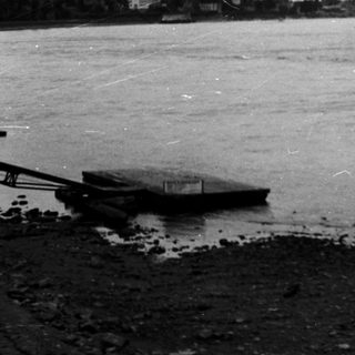 Boat crossing wide river near distant city skyline.