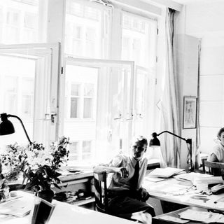 Three people working in a bright, cluttered study.
