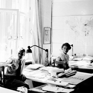 Three people working in a bright, cluttered study.