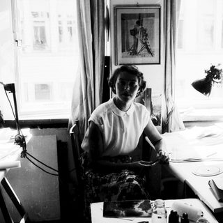 Woman seated at sewing table with fabric and tools.