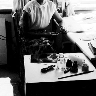 Woman seated at sewing table with fabric and tools.