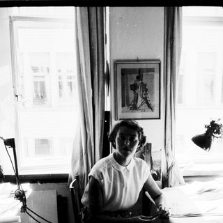 Woman seated at sewing table with fabric and tools.