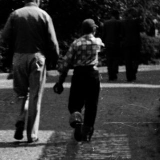 Two adults and child walking on cobblestone path.