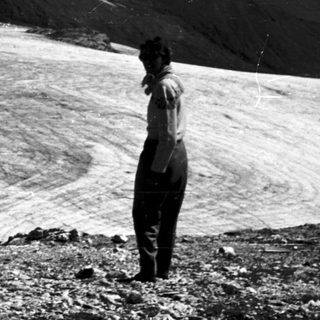 Person standing on rocky terrain near glacier.