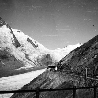 Mountain road with snow-capped peaks and small building.