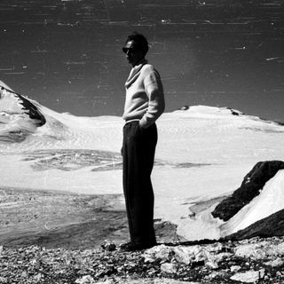 A man stands on rocky terrain near snow-covered mountains.