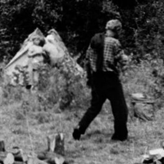 Campsite with tents and people in wooded area.