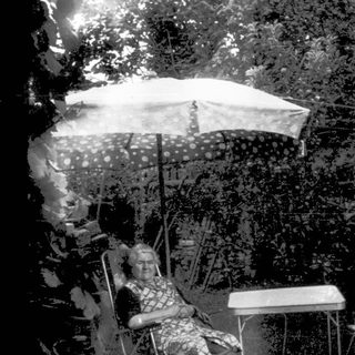 Shirtless boy sitting outside on left, backyard scene with umbrella and chairs.