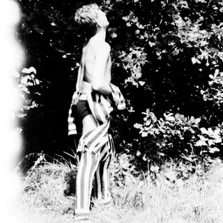 Shirtless person standing outdoors near trees.