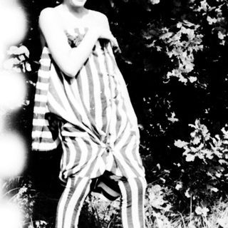Shirtless boy laughing outdoors with striped cloth.