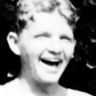 Shirtless boy laughing outdoors with striped cloth.