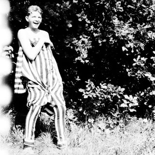Shirtless boy laughing outdoors with striped cloth.