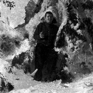 Woman in winter attire standing near snow-covered rocky cliff.