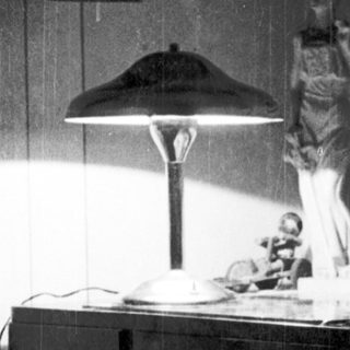 Vintage bedroom scene with statue, desk lamp, and framed art.