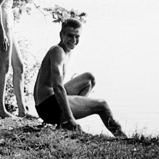 Two people by water, one standing, one kneeling.