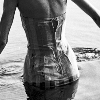 Woman in vintage corset swimsuit standing in shallow water.