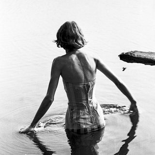 Woman in vintage corset swimsuit standing in shallow water.