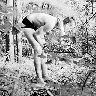 Shirtless person climbing tree in snowy forest.