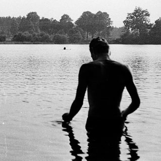 Shirtless person standing in shallow lake water.