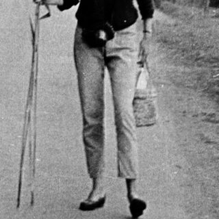 Woman walking outdoors holding fishing rods.