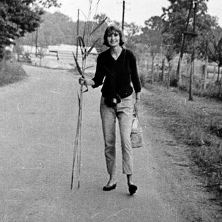 Woman walking outdoors holding fishing rods.