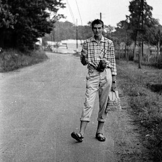 Young man walking on rural road holding cane.