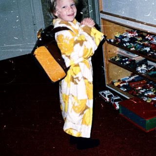 Young child in yellow outfit near toy-filled cabinet.