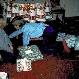 Children opening wrapped holiday gifts indoors.