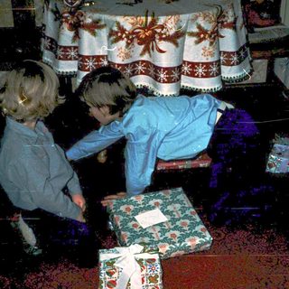 Children opening wrapped holiday gifts indoors.