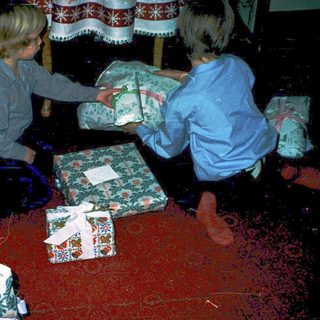 Two children opening holiday gifts indoors.