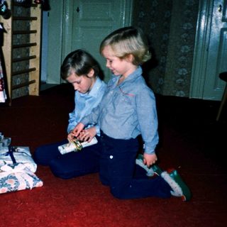 Two children opening wrapped gifts indoors.