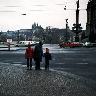 Family crossing street in city with historic background.