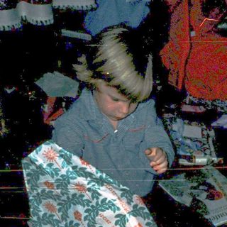 Child unwrapping holiday gifts on floor.